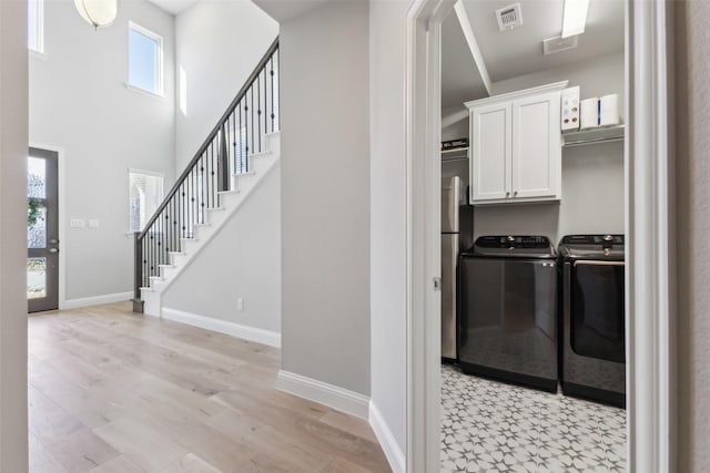 clothes washing area with light hardwood / wood-style flooring, cabinets, and independent washer and dryer