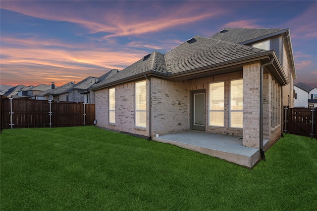 back house at dusk featuring a patio and a lawn