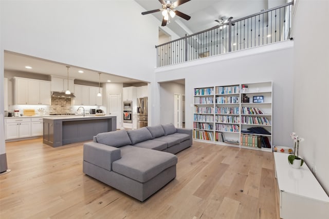 living room with ceiling fan, sink, a towering ceiling, and light hardwood / wood-style floors