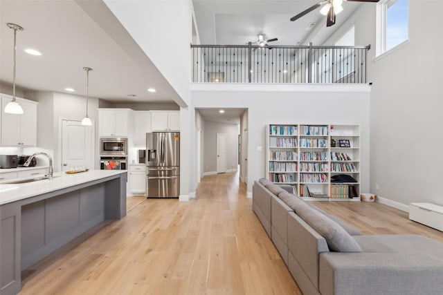 living room with ceiling fan, sink, a high ceiling, and light hardwood / wood-style flooring