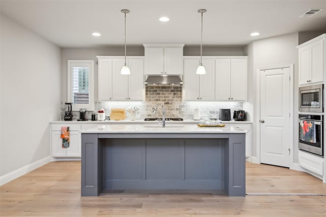 kitchen with appliances with stainless steel finishes, pendant lighting, a center island with sink, white cabinets, and light wood-type flooring