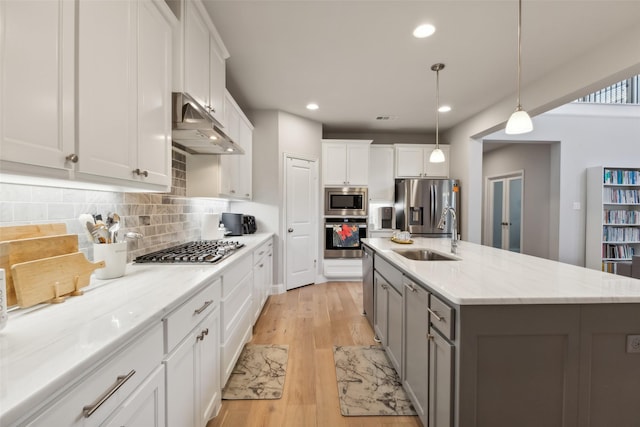 kitchen with pendant lighting, sink, appliances with stainless steel finishes, a kitchen island with sink, and white cabinetry