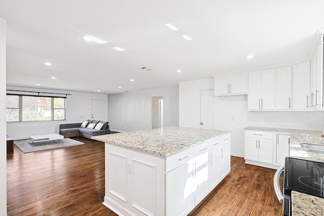 kitchen with white cabinetry, light stone counters, dark hardwood / wood-style flooring, a kitchen island, and range