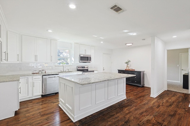 kitchen featuring a center island, white cabinets, light stone countertops, appliances with stainless steel finishes, and dark hardwood / wood-style flooring