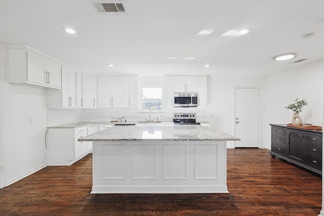 kitchen with white cabinetry, dark hardwood / wood-style flooring, a kitchen island, and stainless steel appliances