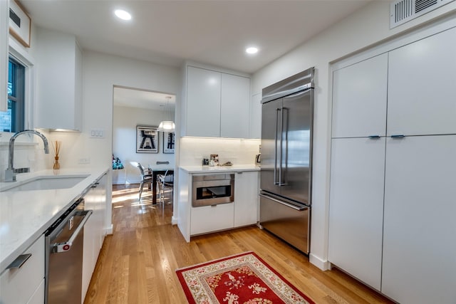 5919 Bordeaux Ave, Dallas, TX 75209 - kitchen featuring stainless steel appliances, modern cabinets, light wood finished floors, white cabinetry, and backsplash