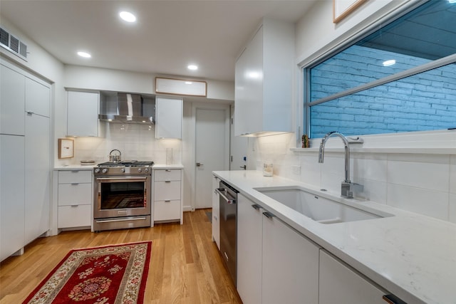 kitchen with sink, white cabinets, wall chimney exhaust hood, stainless steel appliances, and light hardwood / wood-style flooring