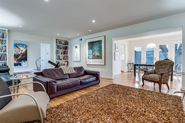 living room with built in shelves, french doors, and light wood-type flooring