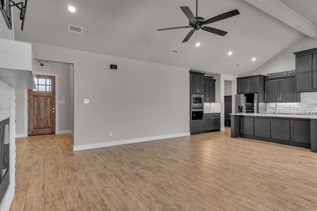 kitchen featuring light wood-type flooring, ceiling fan, stainless steel appliances, beam ceiling, and decorative backsplash