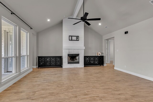 unfurnished living room with beam ceiling, a large fireplace, light hardwood / wood-style flooring, and a healthy amount of sunlight