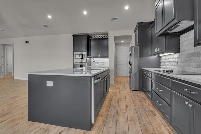 kitchen featuring sink, backsplash, stainless steel appliances, a center island with sink, and light wood-type flooring