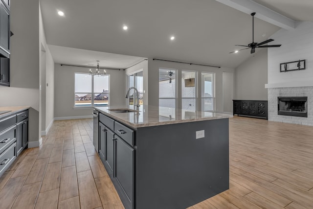 kitchen with ceiling fan with notable chandelier, a kitchen island with sink, sink, and light stone countertops