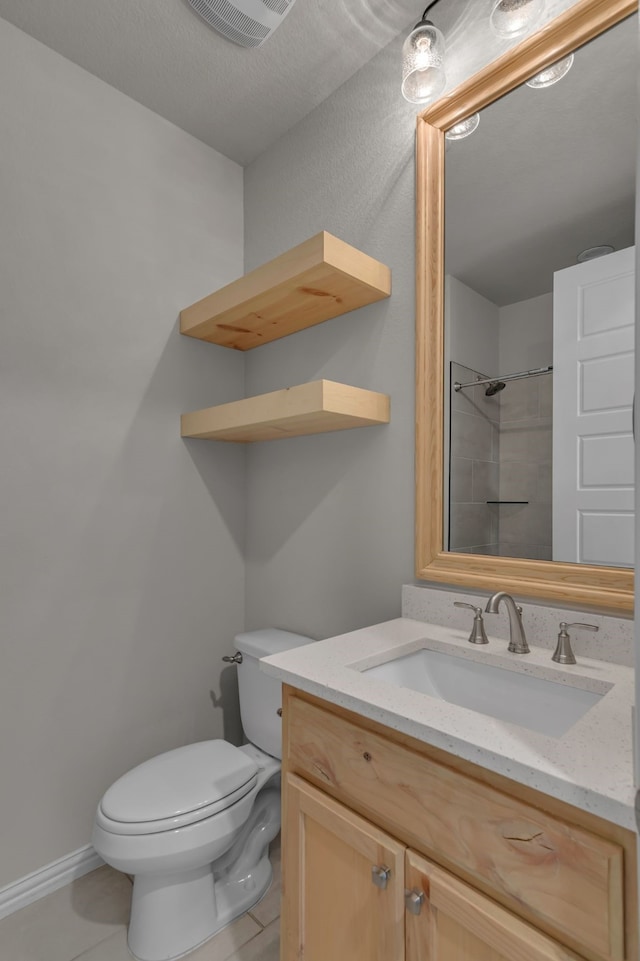 bathroom with tile patterned flooring, vanity, tiled shower, and toilet