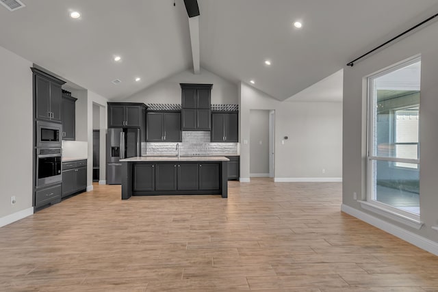 kitchen with vaulted ceiling with beams, light wood-type flooring, a kitchen island with sink, and appliances with stainless steel finishes