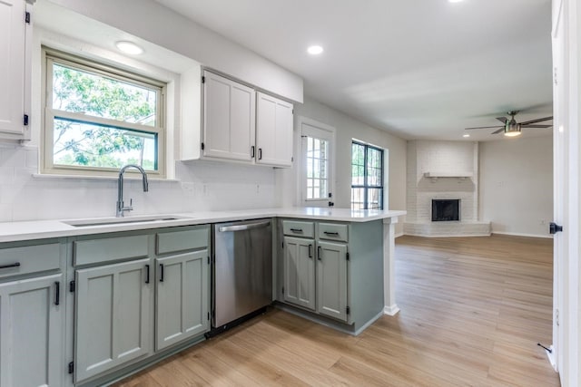 kitchen with dishwasher, sink, backsplash, a brick fireplace, and light hardwood / wood-style flooring