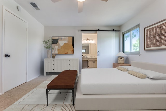 carpeted bedroom featuring ensuite bathroom, a barn door, and ceiling fan