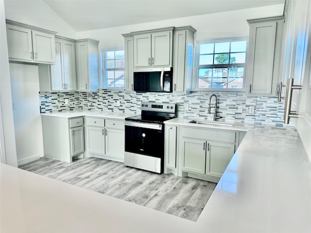 kitchen with sink, backsplash, light hardwood / wood-style floors, lofted ceiling, and appliances with stainless steel finishes