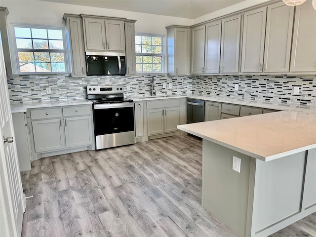 kitchen featuring tasteful backsplash, kitchen peninsula, light wood-type flooring, and appliances with stainless steel finishes