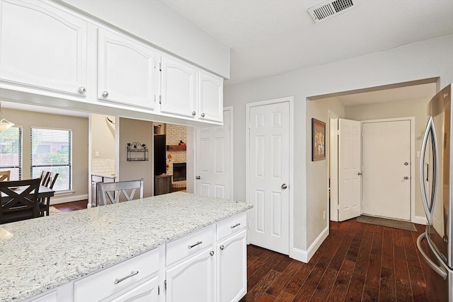 kitchen featuring stainless steel refrigerator, a fireplace, white cabinets, light stone counters, and dark wood-type flooring