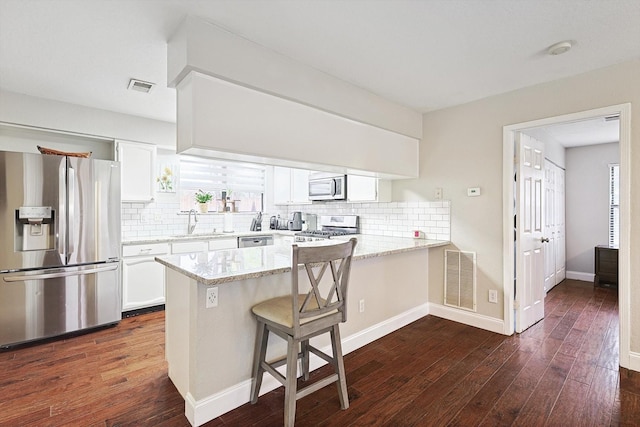 kitchen featuring sink, white cabinets, a kitchen bar, kitchen peninsula, and stainless steel appliances