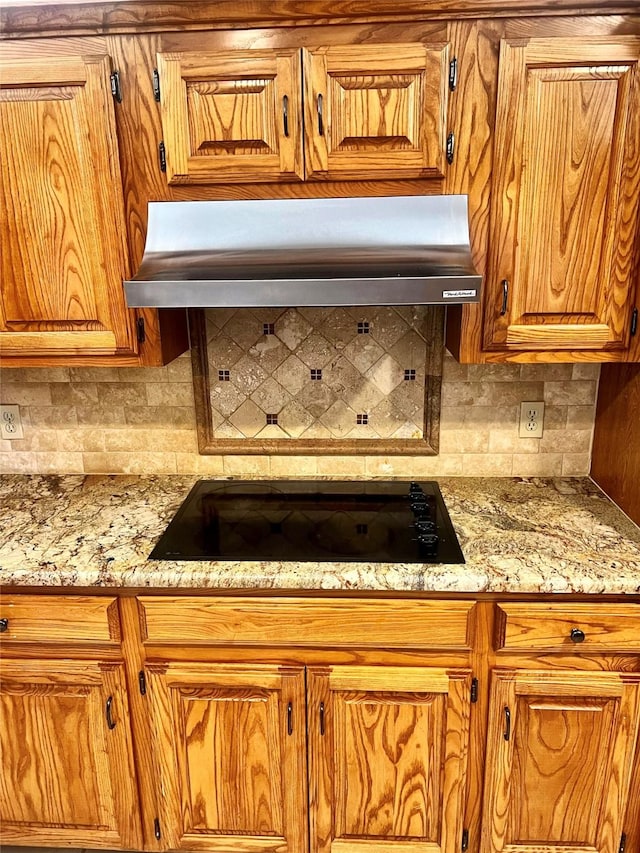 kitchen with light stone counters, black electric stovetop, and backsplash