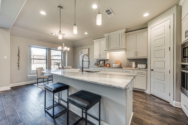 kitchen with decorative light fixtures, a center island with sink, white cabinetry, and dark wood-type flooring