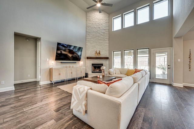 living room featuring a stone fireplace, dark wood-type flooring, ceiling fan, and plenty of natural light