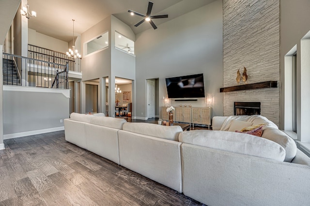 living room with hardwood / wood-style floors, ceiling fan with notable chandelier, a fireplace, and a high ceiling