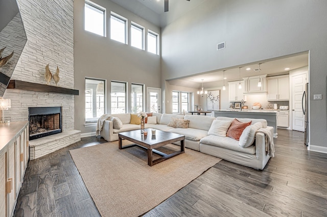 living room featuring a fireplace, a towering ceiling, dark wood-type flooring, and ceiling fan with notable chandelier