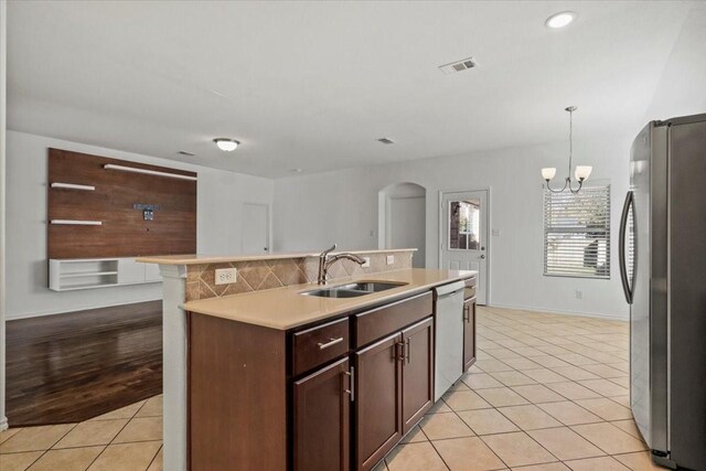 kitchen with dishwasher, sink, hanging light fixtures, an island with sink, and stainless steel refrigerator