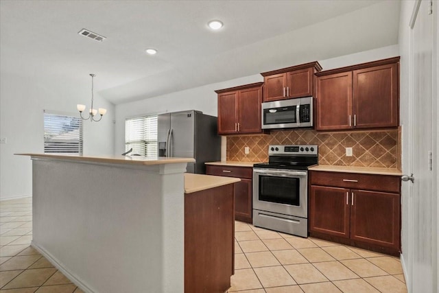 kitchen featuring a notable chandelier, vaulted ceiling, a kitchen island with sink, light tile patterned floors, and appliances with stainless steel finishes