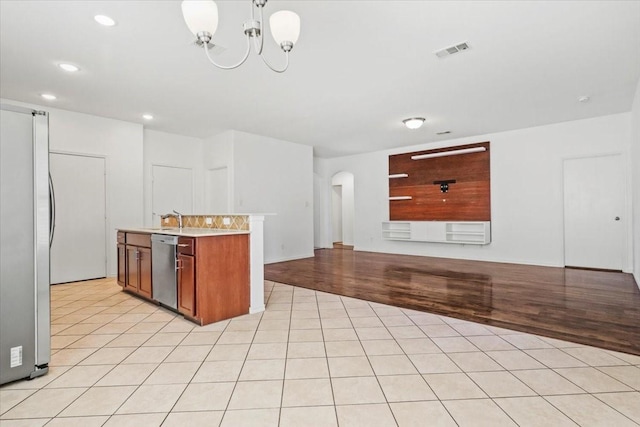 kitchen with appliances with stainless steel finishes, an inviting chandelier, light hardwood / wood-style flooring, and pendant lighting