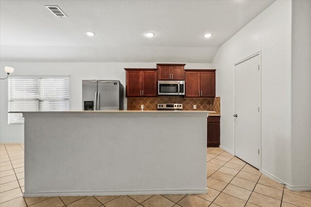 kitchen featuring lofted ceiling, decorative backsplash, light tile patterned floors, a kitchen island, and stainless steel appliances