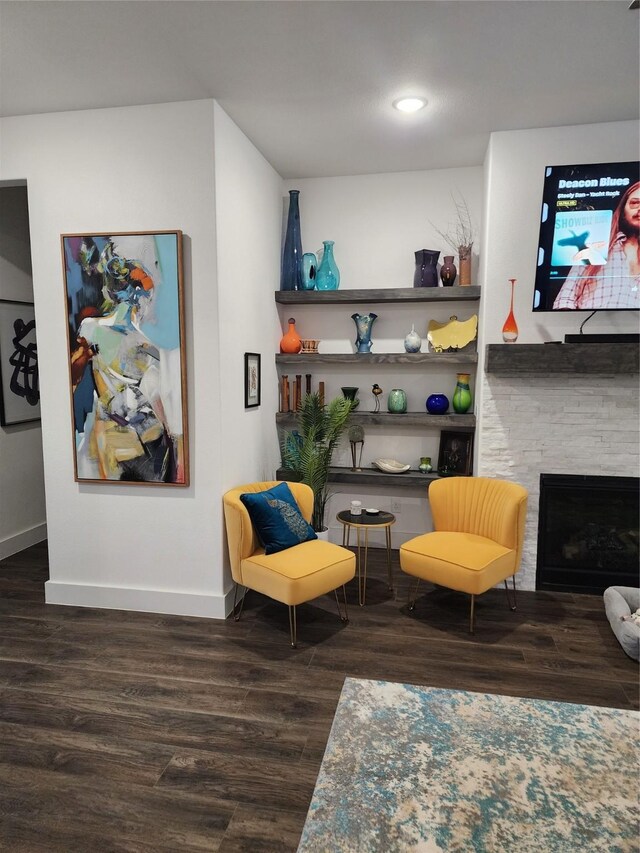 living room with a stone fireplace, dark wood-type flooring, and ceiling fan