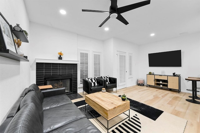 living room featuring hardwood / wood-style floors, ceiling fan, and a tiled fireplace