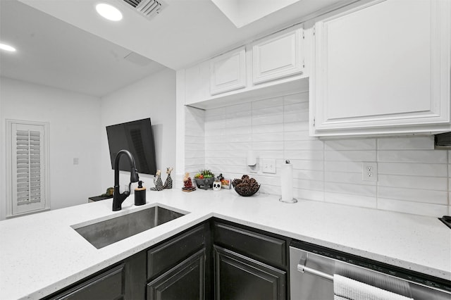 kitchen with light stone countertops, tasteful backsplash, stainless steel dishwasher, sink, and white cabinetry