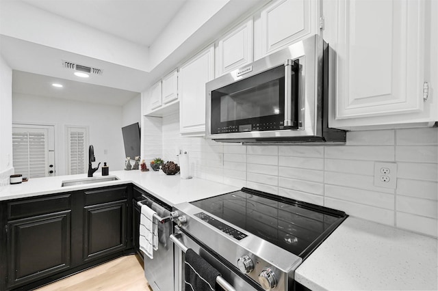 kitchen featuring sink, appliances with stainless steel finishes, decorative backsplash, white cabinets, and light wood-type flooring