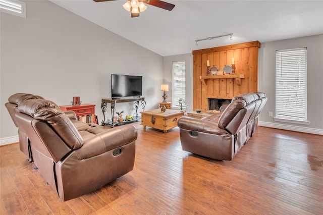 living room with lofted ceiling, hardwood / wood-style floors, track lighting, and a large fireplace