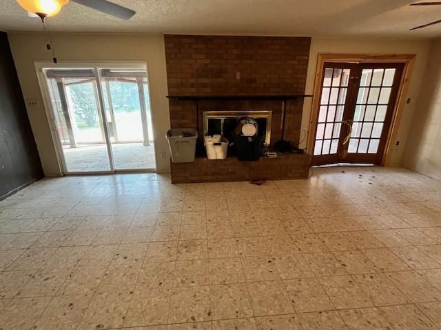 unfurnished living room with french doors, ceiling fan, a fireplace, and a textured ceiling