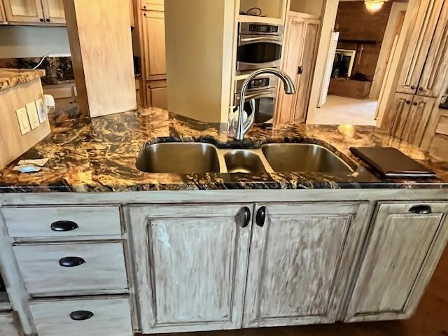 kitchen with stainless steel oven, light brown cabinetry, sink, and dark stone countertops