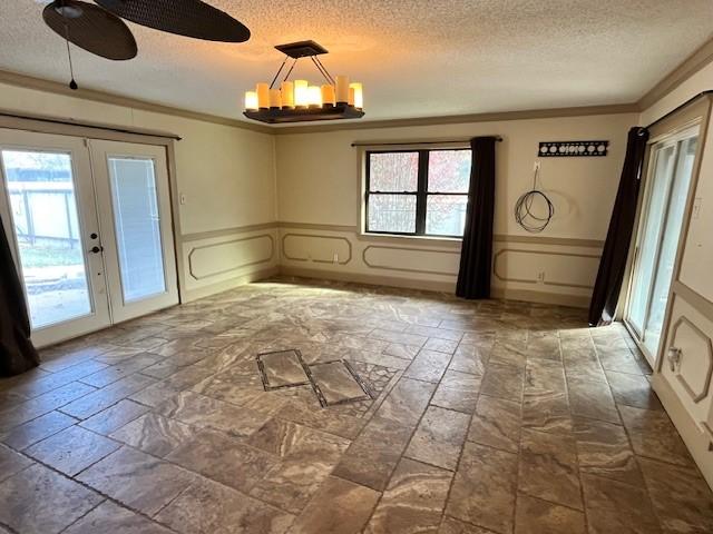 unfurnished dining area featuring a chandelier, ornamental molding, french doors, and a textured ceiling