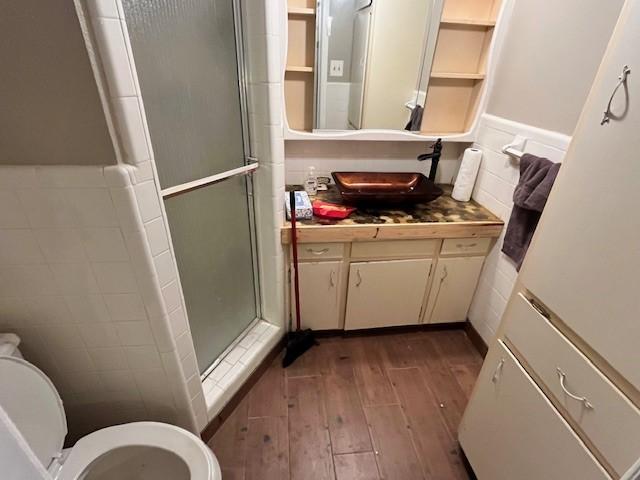 bathroom featuring hardwood / wood-style flooring, tile walls, an enclosed shower, vanity, and toilet