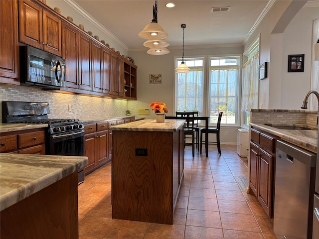 kitchen featuring appliances with stainless steel finishes, ornamental molding, sink, decorative light fixtures, and a center island