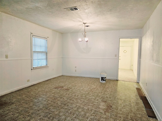 empty room with a textured ceiling and a chandelier