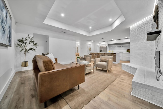 living room with a tray ceiling and light hardwood / wood-style flooring