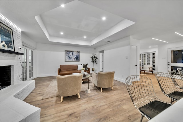 living room featuring a raised ceiling, a fireplace, and light hardwood / wood-style floors