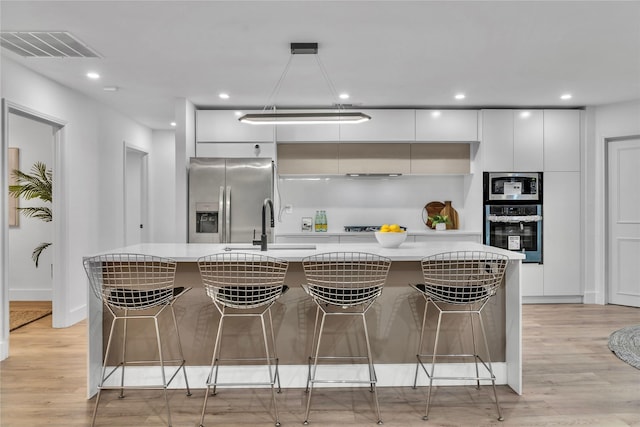 kitchen with a kitchen bar, appliances with stainless steel finishes, a kitchen island with sink, light hardwood / wood-style flooring, and white cabinets