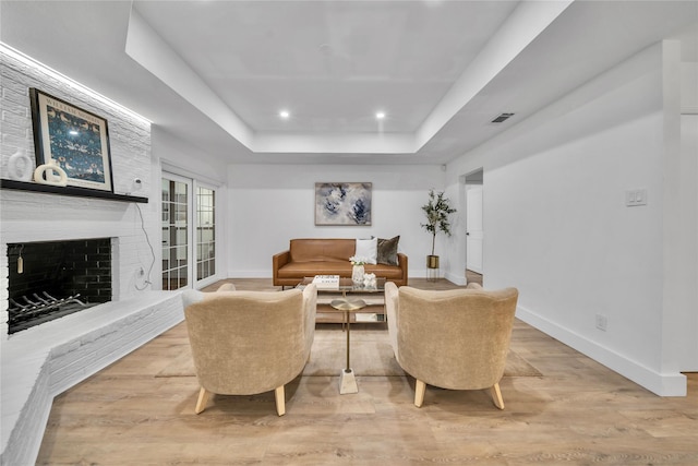 living room featuring a raised ceiling, light wood-type flooring, and a fireplace