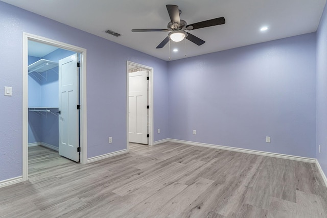 unfurnished bedroom with a spacious closet, a closet, ceiling fan, and light hardwood / wood-style flooring