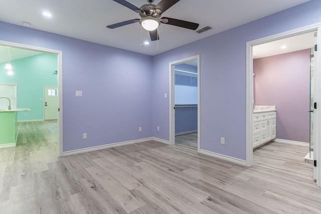 unfurnished bedroom with ensuite bathroom, a walk in closet, ceiling fan, light wood-type flooring, and a closet